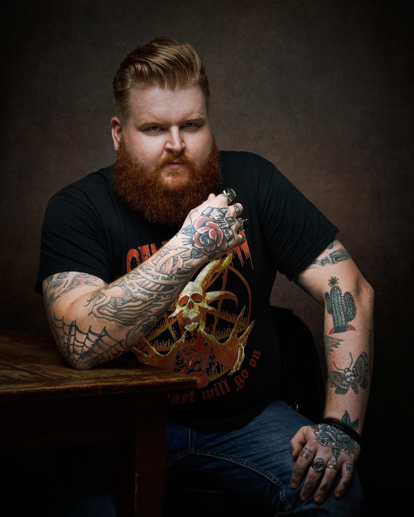 Porträtt av man med tatueringar i studio med mörk bakgrund